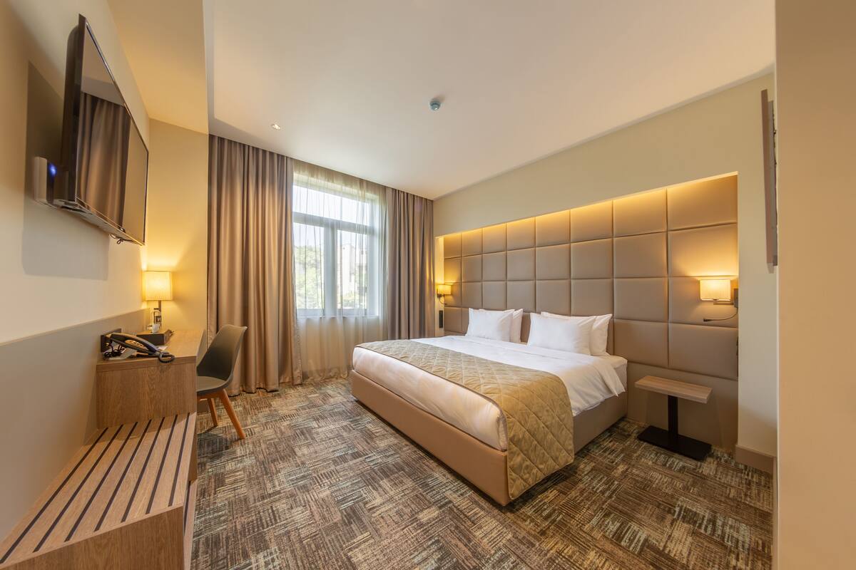 A hotel room with a large bed, a desk with a telephone, a chair, and a television mounted on the wall.