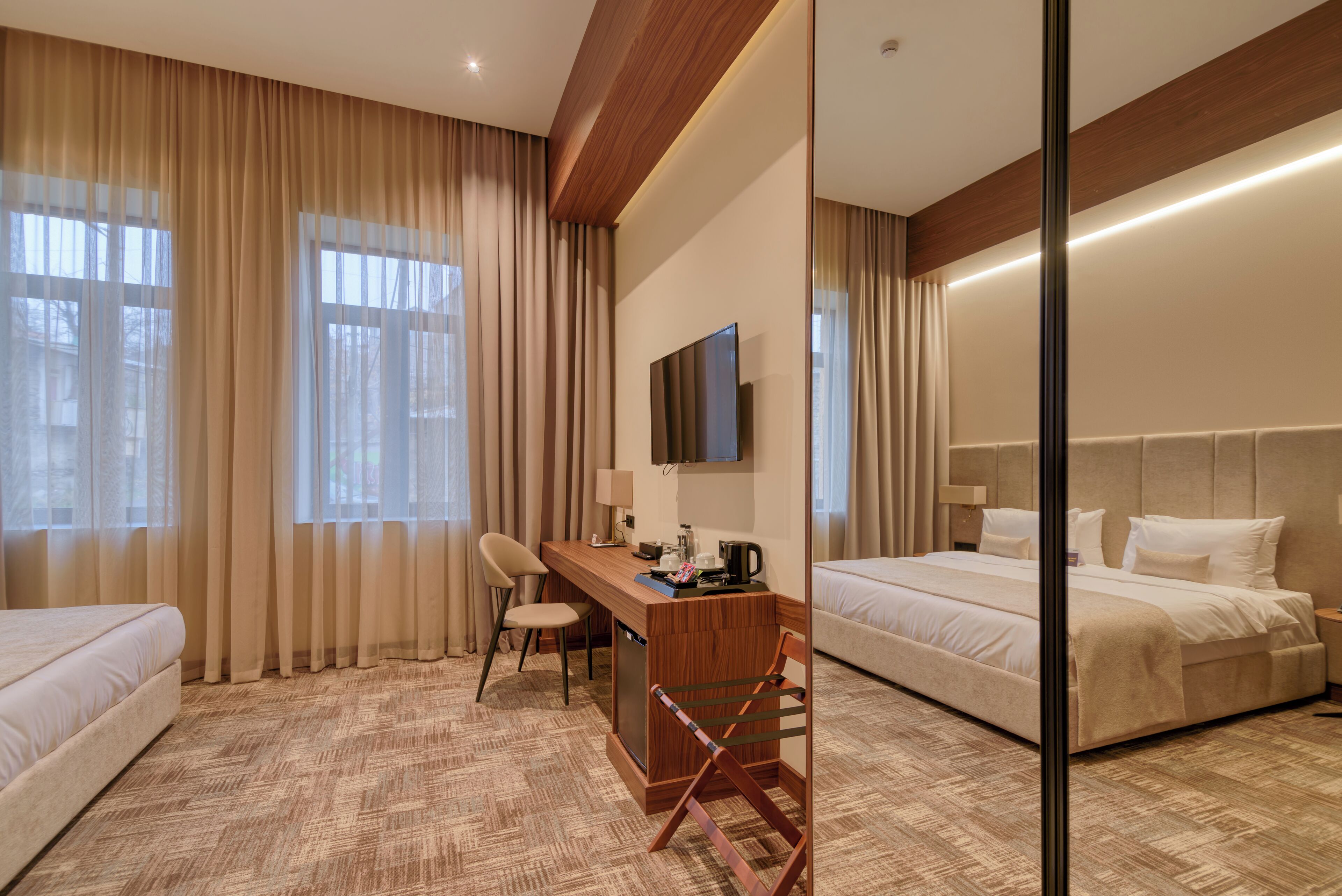 Habitación de hotel con dos camas, un escritorio, una silla, un televisor y un amplio ventanal con cortinas.