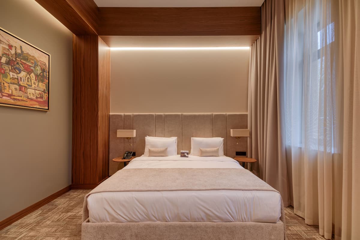 A large, neatly made bed in a hotel room with a wooden headboard, two bedside tables with lamps, and a painting on the wall.