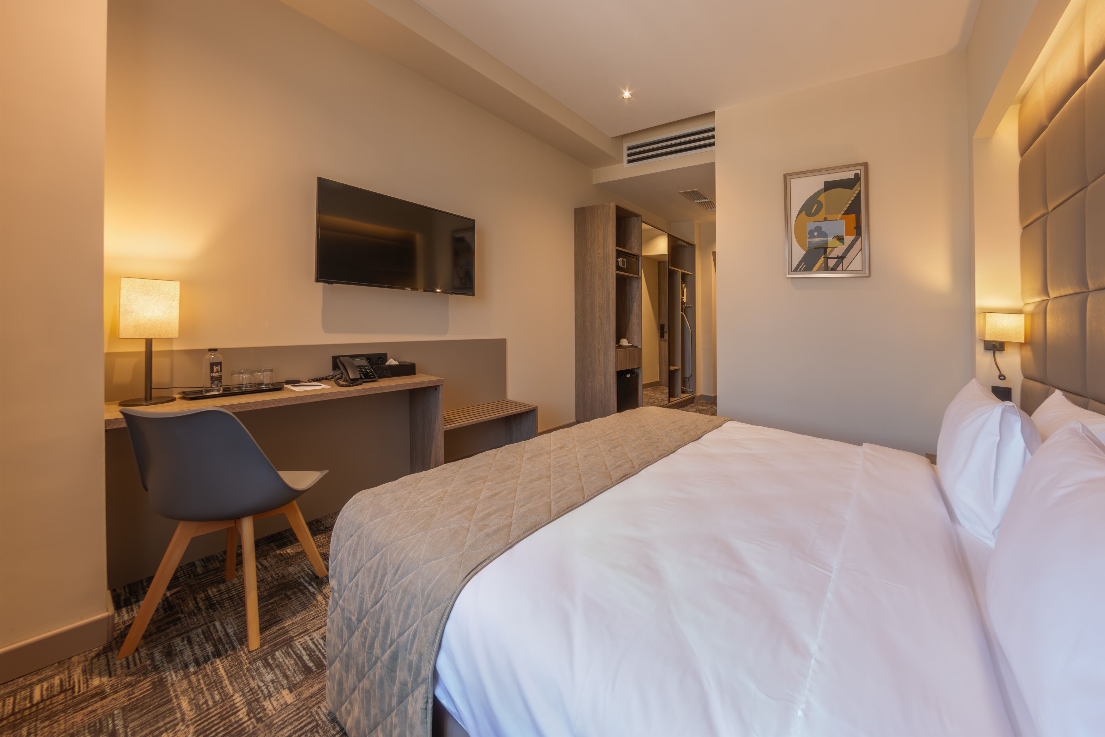 A hotel room with a bed, a desk, a chair, a television, and a shower area.