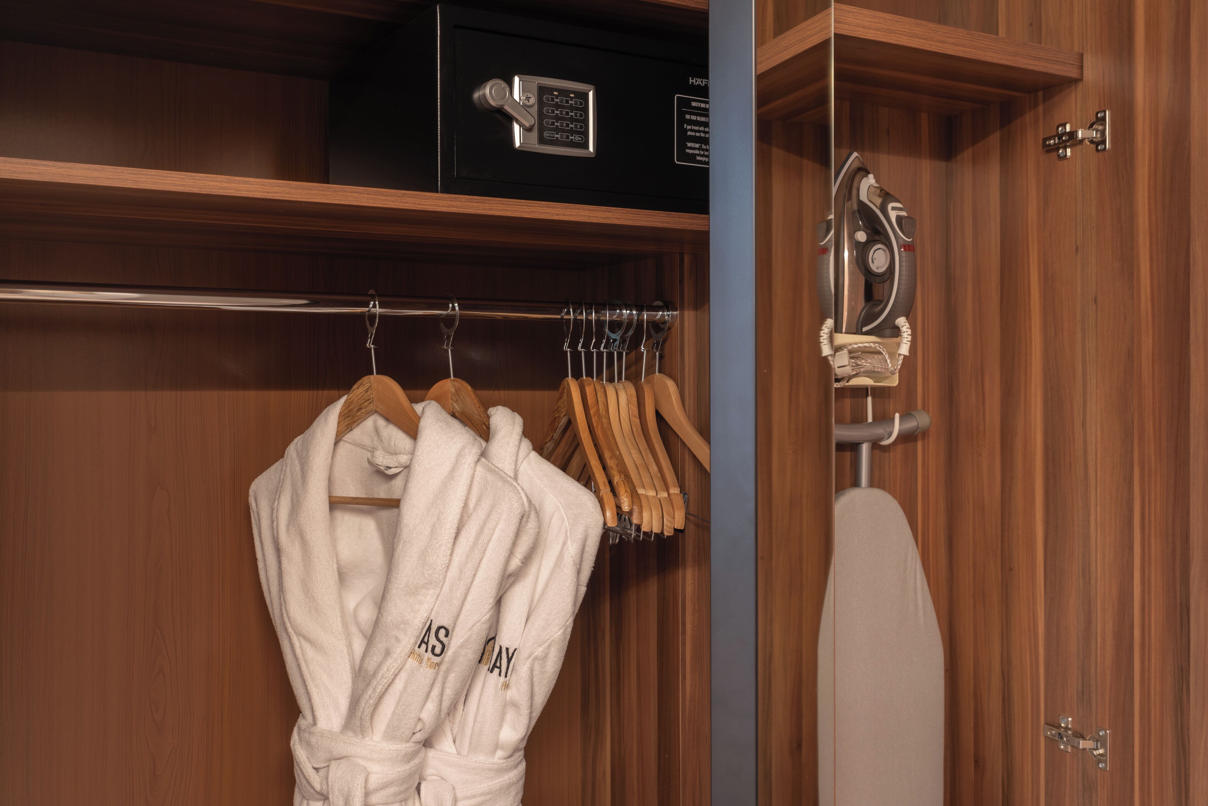 A wooden closet with a hanging rack holding bathrobes and a towel.