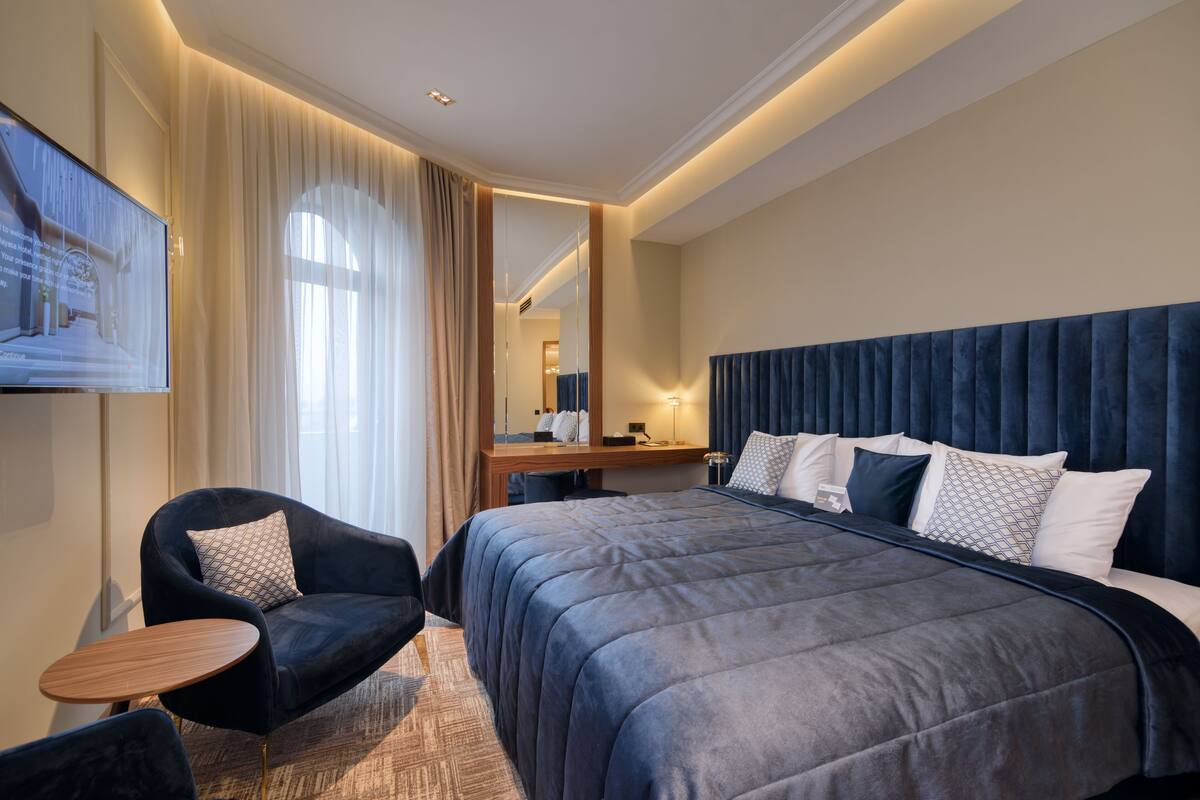 A modern hotel room with a large bed, a desk, a chair, and a TV.