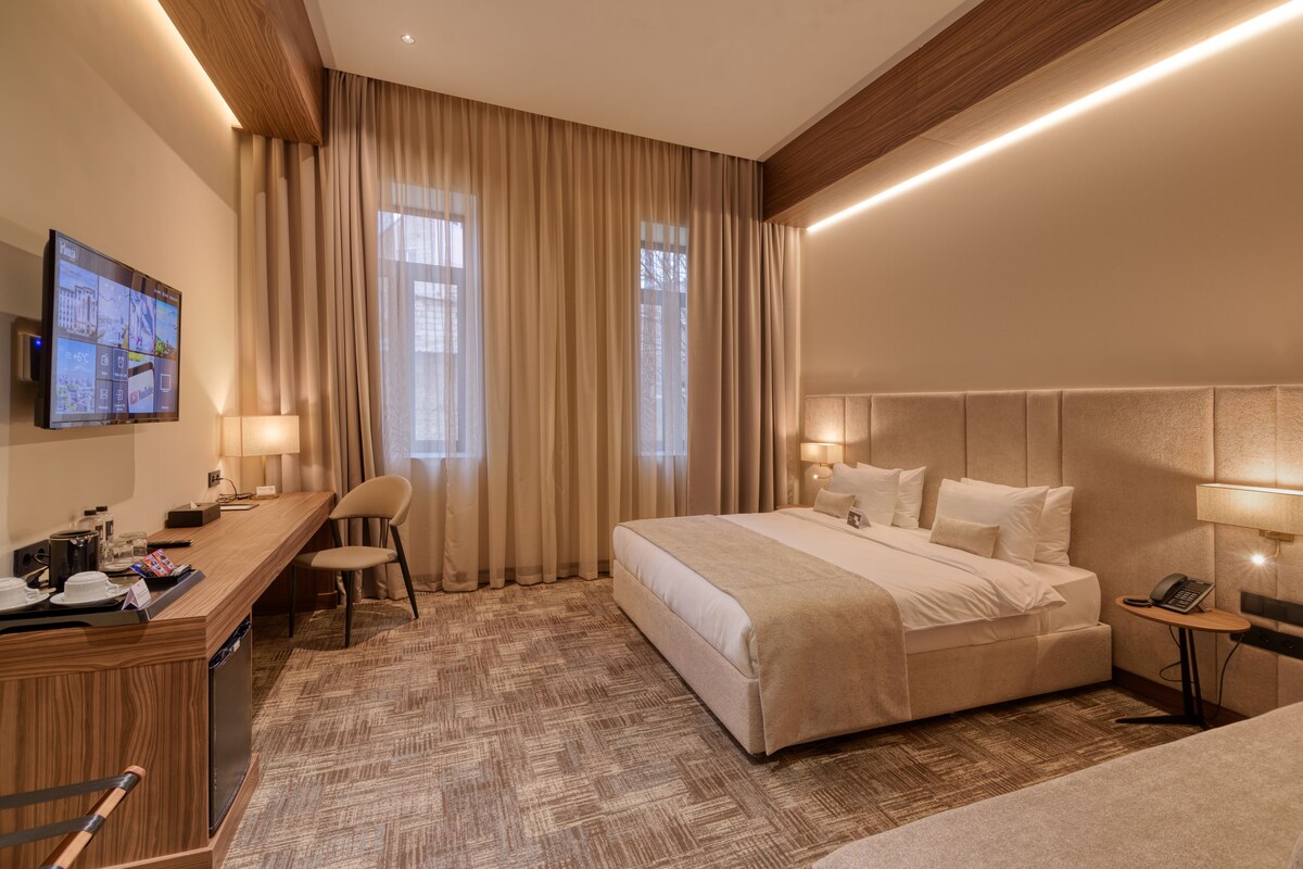 A hotel room with a large bed, a desk with a chair, a television, and a small table with a phone.