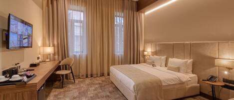 A hotel room with a large bed, a desk with a chair, a television, and a small table with a phone.