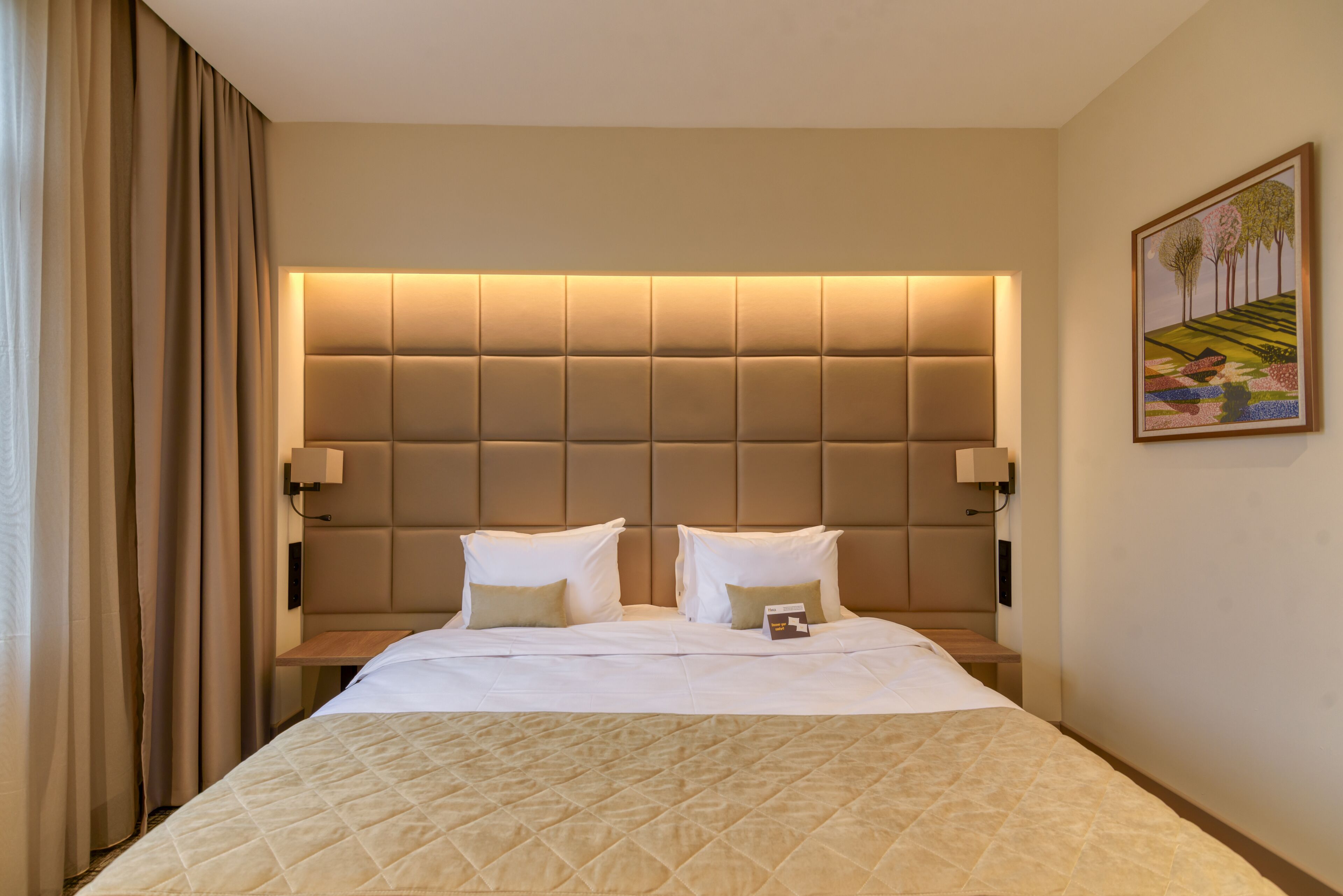 Ein Hotelzimmer mit einem großen Bett, einem gepolsterten Kopfteil, zwei Nachttischen und einem Bild an der Wand.