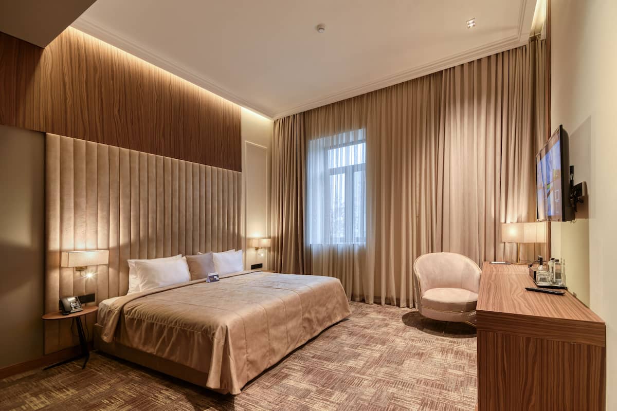 A modern hotel room with a large bed, a desk, a chair, and a TV.