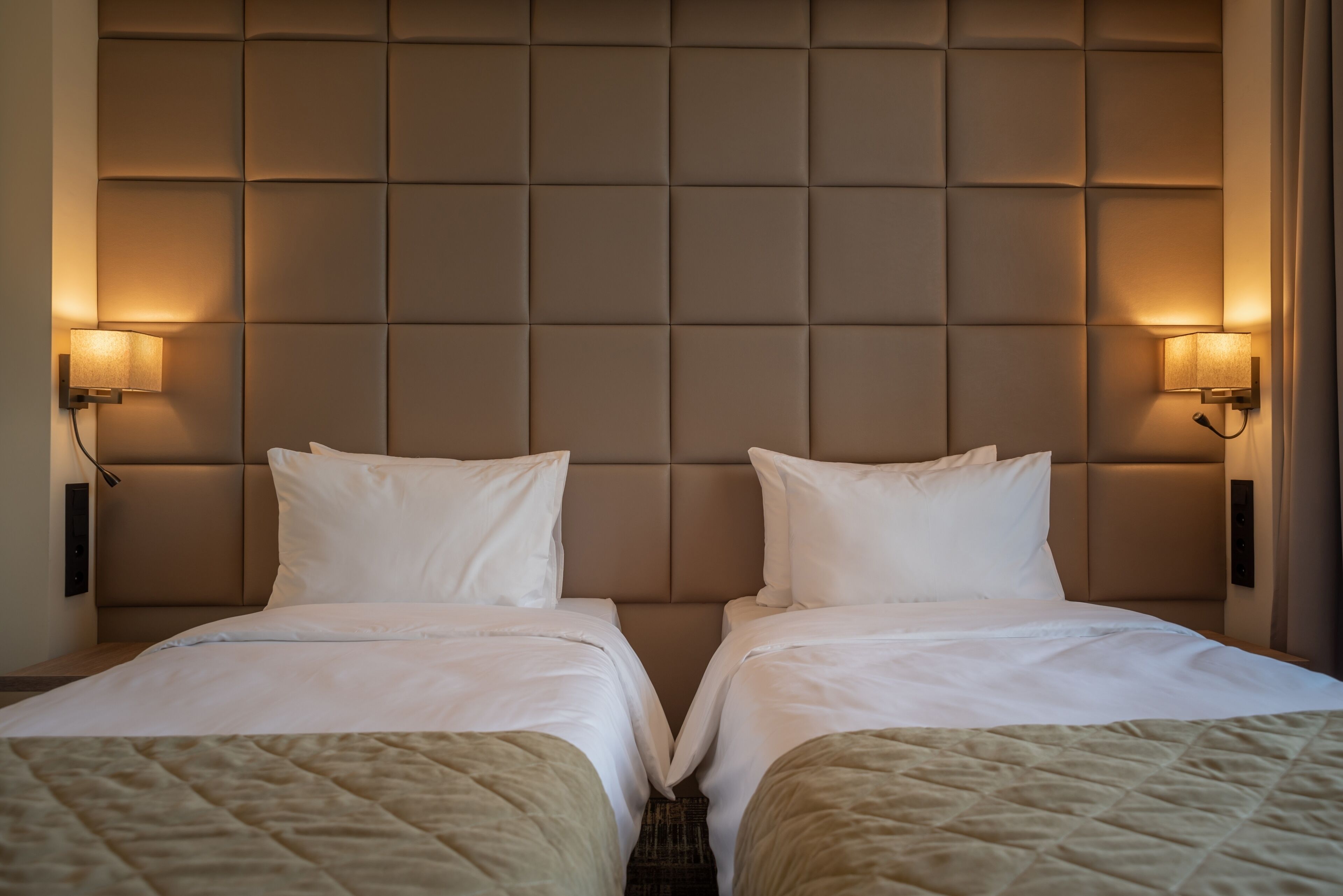Una habitación de hotel con dos camas, cabecero acolchado y lámparas de pared.
