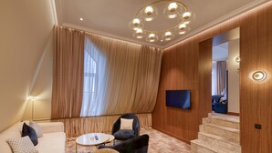 Una habitación de hotel moderna con sofá, sillones, una mesita de centro, televisión y una escalera.