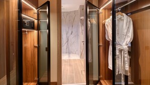 Un baño moderno con ducha de mármol, armarios de madera y una bata colgada en un perchero.