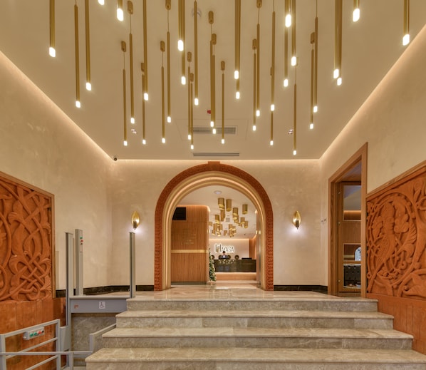 A hotel lobby with a marble staircase, a reception desk, and a modern chandelier.