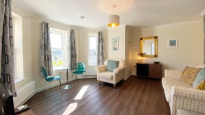 A spacious living room with a sofa, armchair, and a glass table. - Spacious, one bedroom, pet friendly apartment with large terrace overlooking the town. (Torquay)