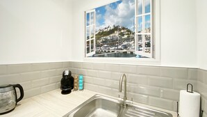 A kitchen with a stainless steel sink, a coffee maker, and a window with a view of a marina. - Spacious, one bedroom, pet friendly apartment with large terrace overlooking the town. (Torquay)