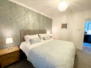Une chambre à coucher avec un grand lit, une table de chevet avec des tiroirs, une lampe et un lustre.