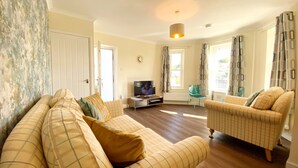 A living room with a sofa, armchairs, a TV, and a window with curtains. - Spacious, one bedroom, pet friendly apartment with large terrace overlooking the town. (Torquay)