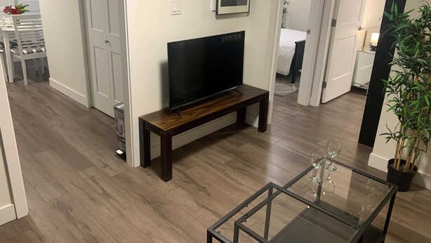 Un soggiorno moderno con una televisione a schermo piatto su una panca di legno, un tavolino da caffè in vetro e una pianta in vaso.