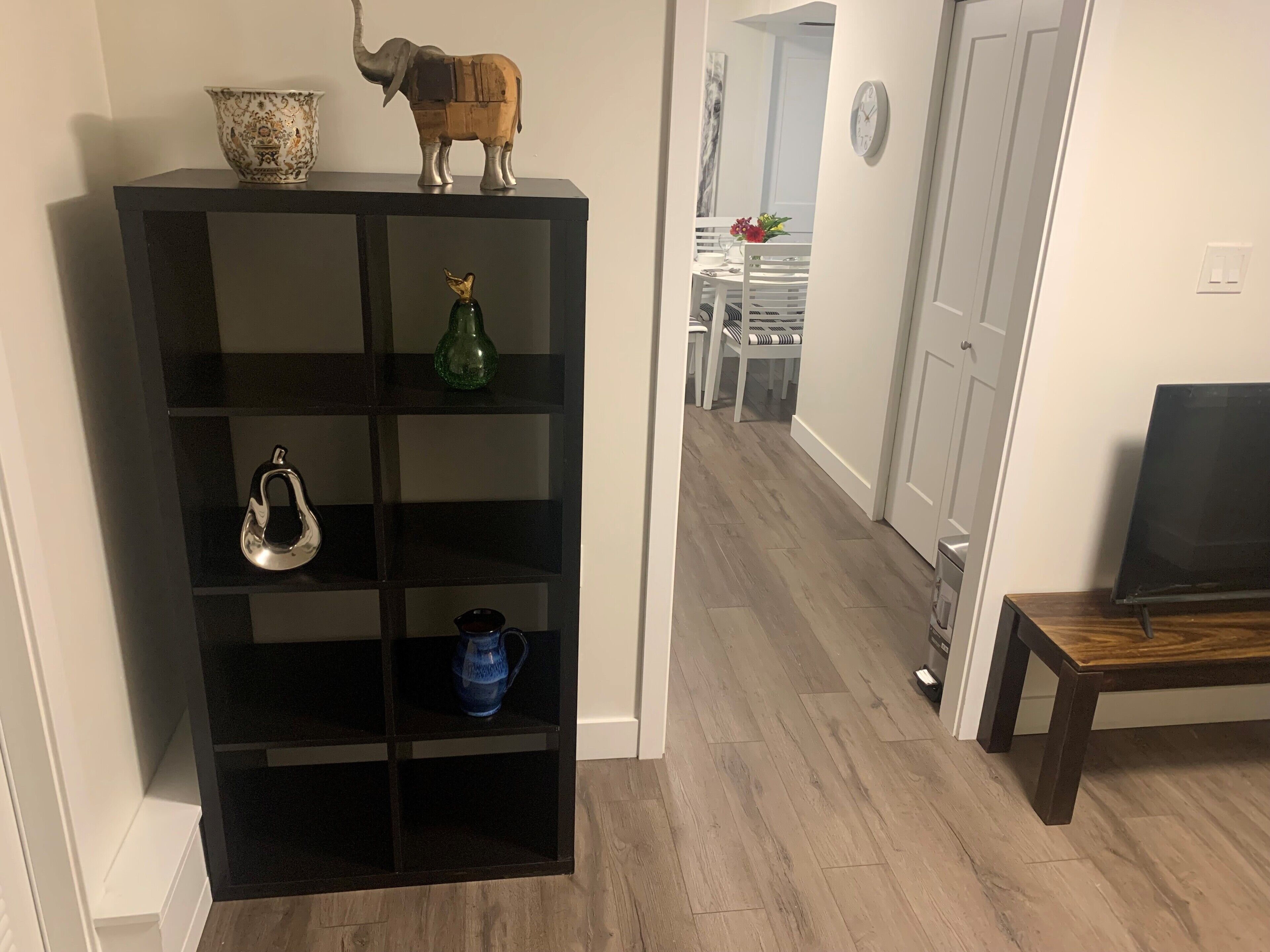 A black shelving unit with decorative items, a wooden elephant figure, a green vase, a silver teapot, and a blue pitcher.