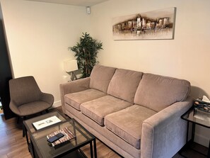 A living room with a sofa, armchair, coffee table, and a painting on the wall. - Modern, stylish, bright and peaceful 2 Bedroom New Suite. Fully licensed (Burnaby)