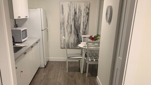 Una cucina moderna con mobili bianchi, un forno a microonde, un frigorifero e un'area pranzo con un tavolo e sedie bianche.