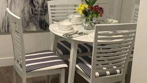 Un'area pranzo con un tavolo rotondo, sedie bianche con cuscini a righe, un vaso con fiori e un grande quadro astratto appeso al muro.