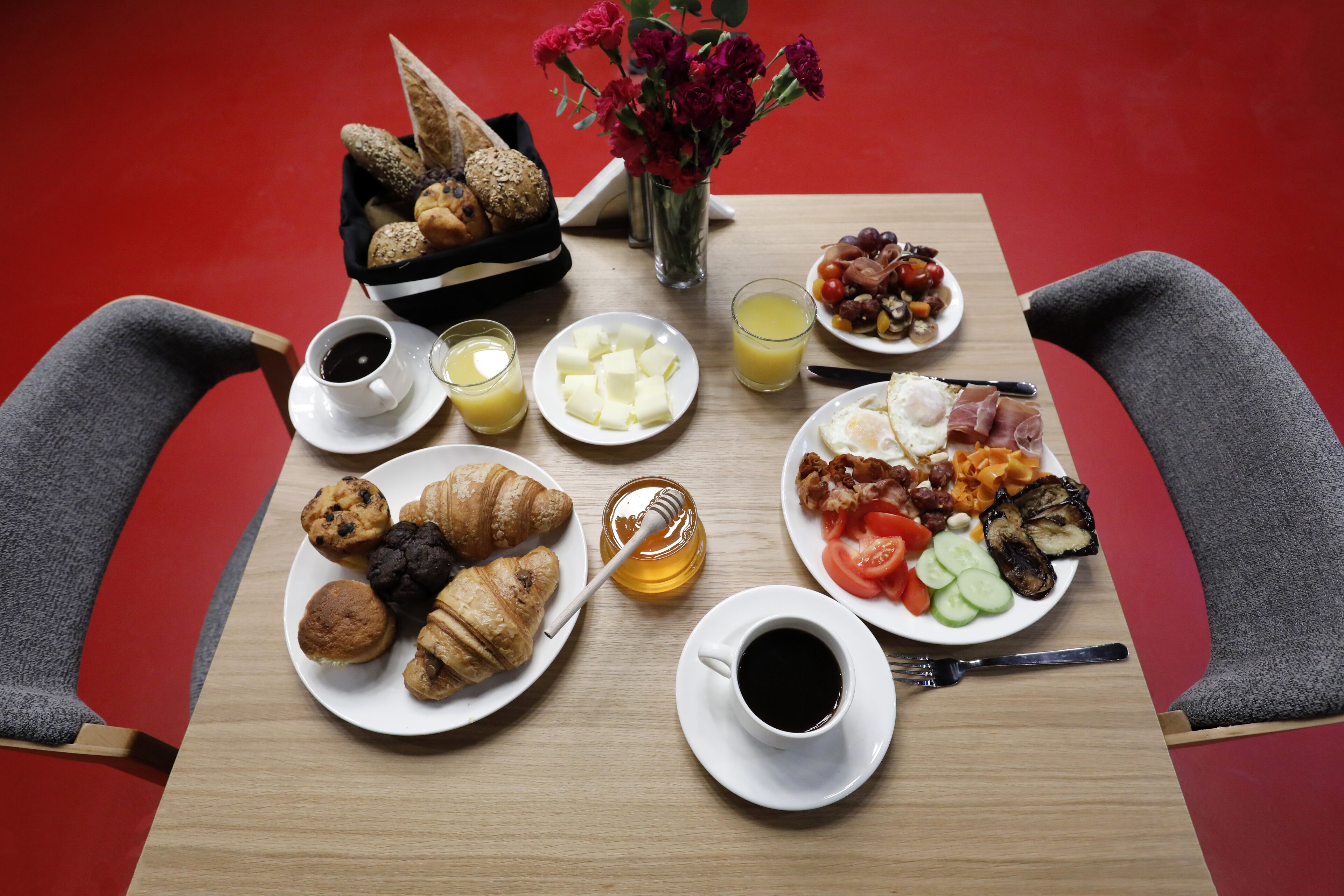 A breakfast table with croissants, eggs, tomatoes, and a variety of spreads.