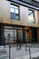 Un edificio moderno con fachada de madera, ventanas amplias y una escalera con barandillas de metal.