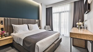 Een moderne hotelkamer met een groot bed, nachtkastjes, een bureau en een aan de muur bevestigde televisie.