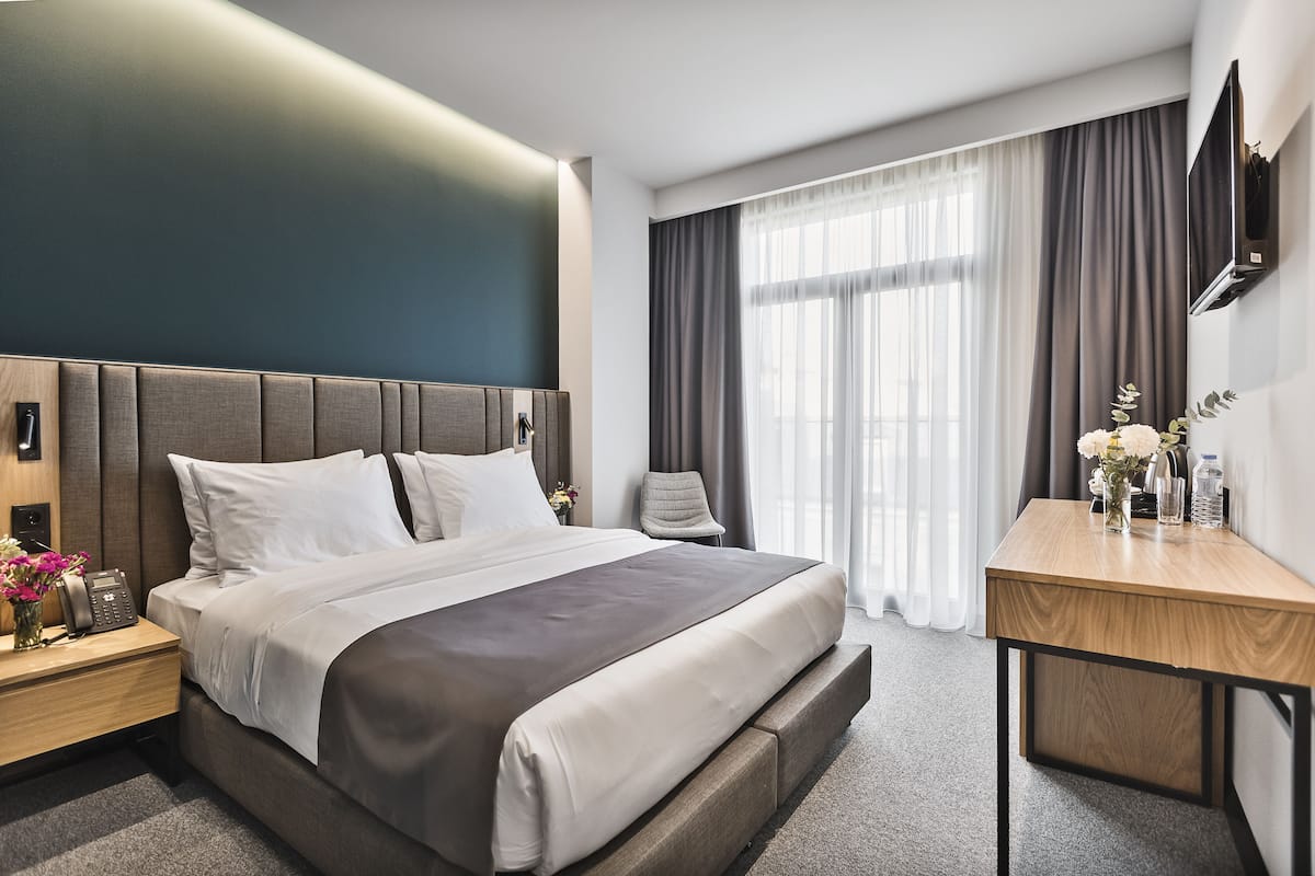 A modern hotel room with a large bed, bedside tables, a desk, and a TV mounted on the wall.