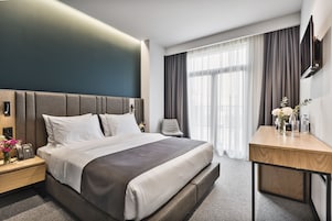 Una habitación de hotel moderna con una cama grande, mesitas de noche, un escritorio y un televisor montado en la pared.