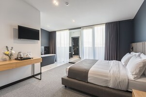 Habitación de hotel moderna con una cama grande, un escritorio con televisor de pantalla plana, un baño y vistas a la ciudad.