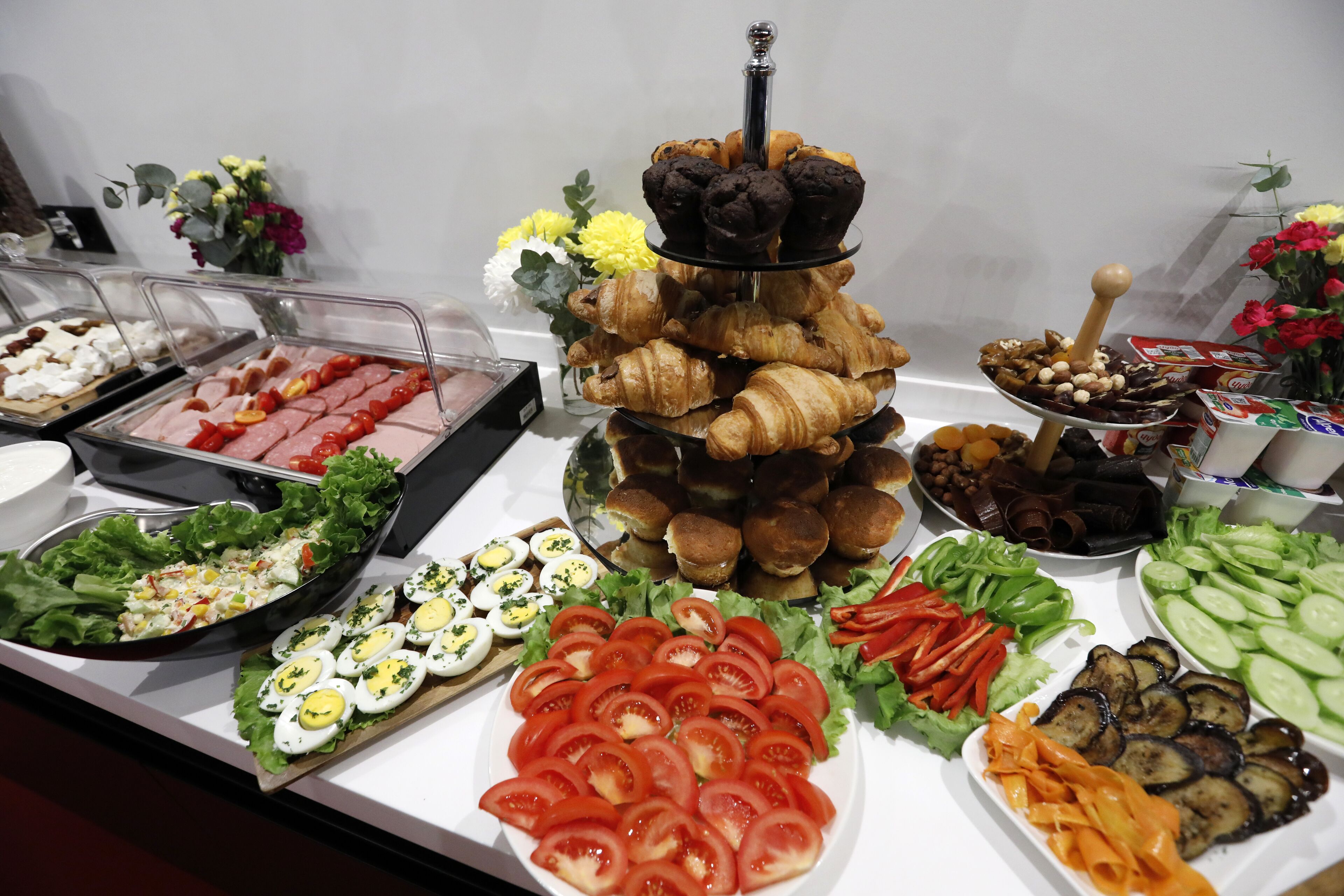 Un bufé con diferentes opciones de comida, incluyendo ensaladas, huevos, tomates y productos de pastelería.