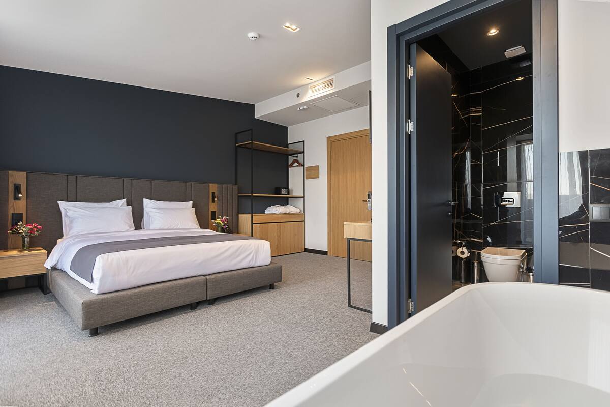 A modern bedroom with a large bed, a walk-in closet, and a separate bathroom with a bathtub.