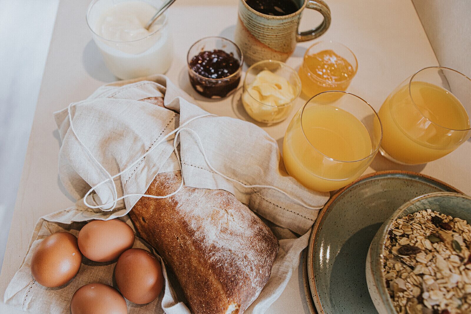 Una mesa con desayuno: huevos, pan, mantequilla, mermelada y zumo de naranja.