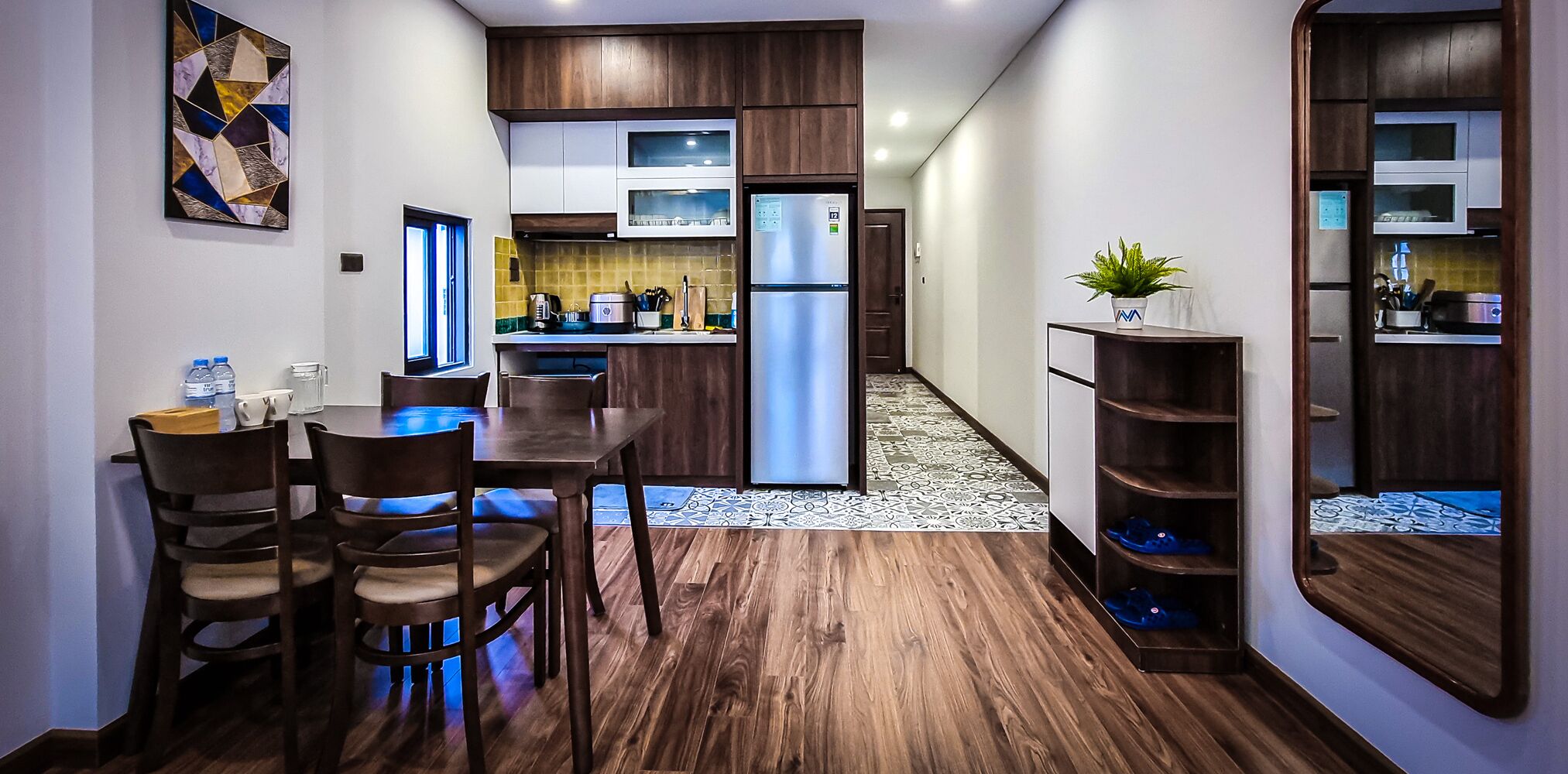 A modern kitchen with wooden cabinets, a stainless steel refrigerator, and a dining area with a table and chairs.