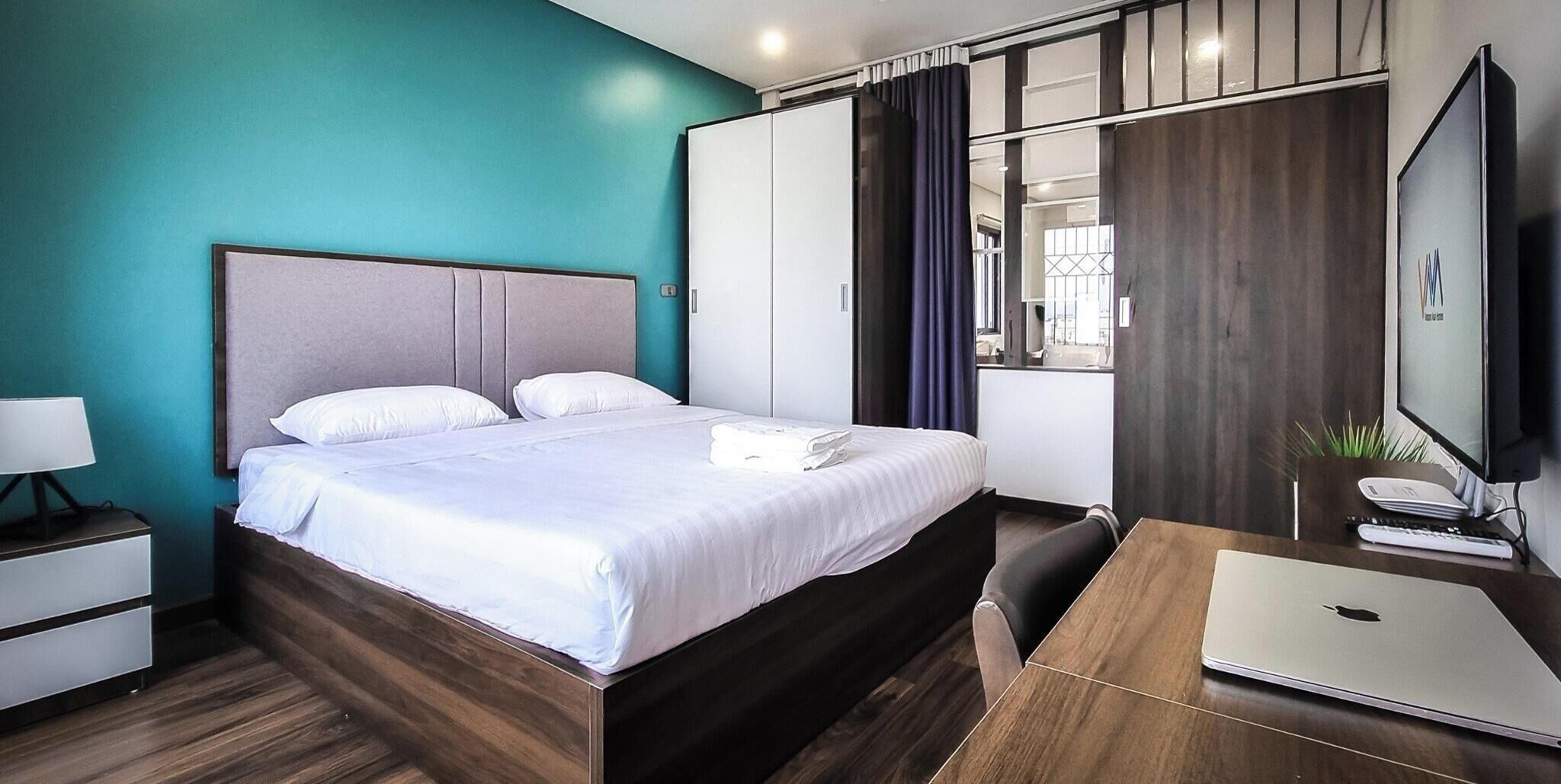 A modern hotel room with a bed, a desk with a laptop, a TV, and a wardrobe.