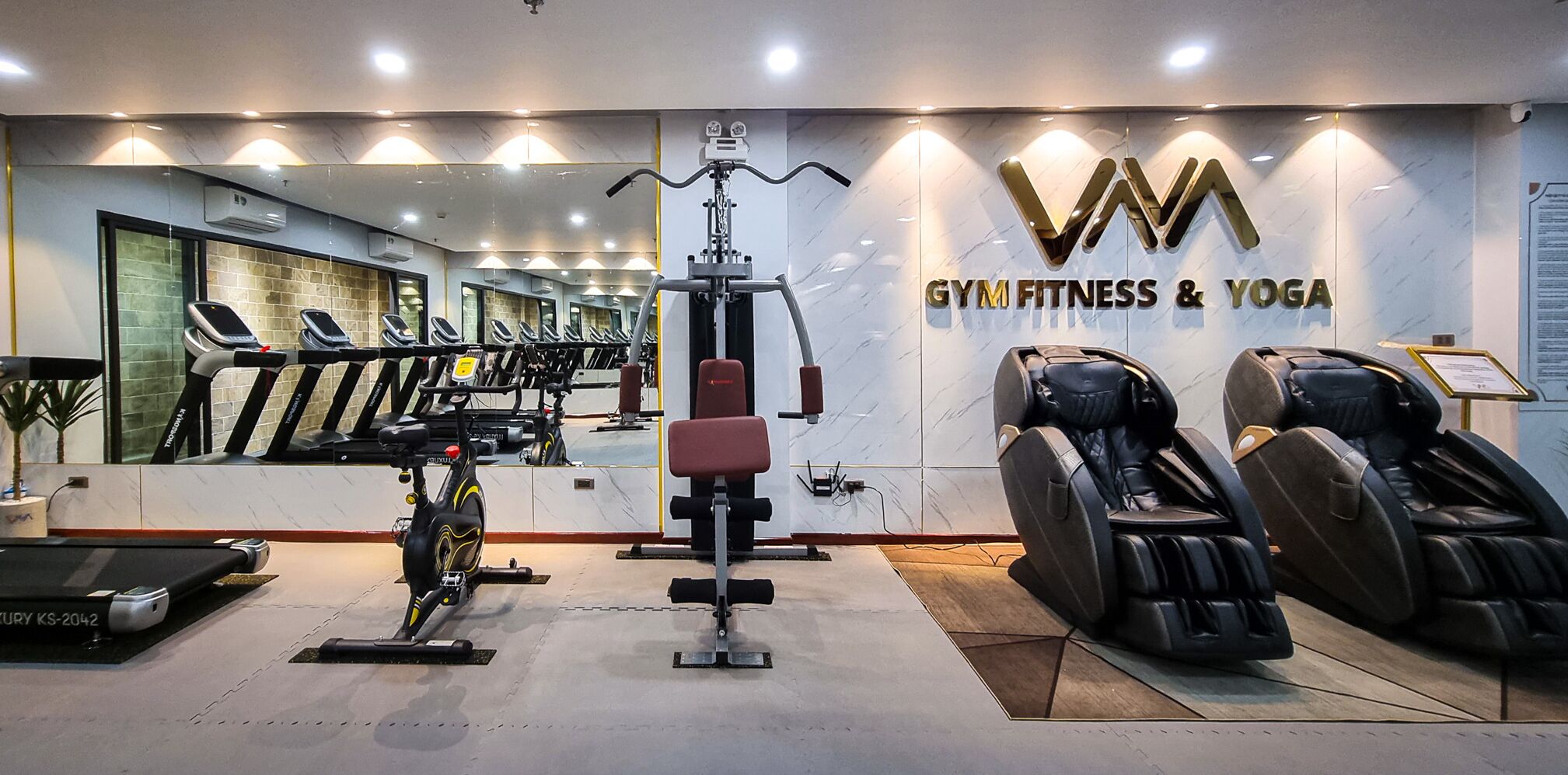 Ein Fitnessraum mit Trainingsgeräten, Laufband und Massagesessel.