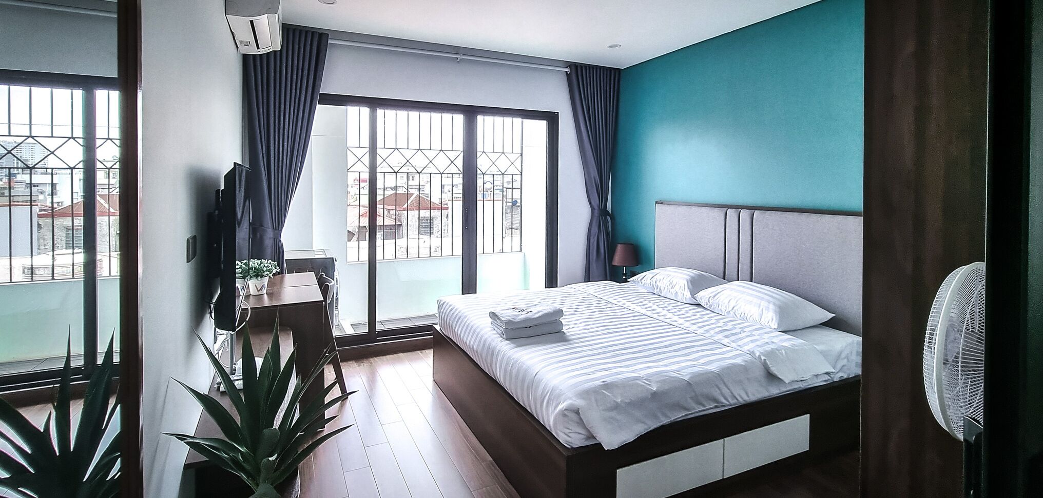Une chambre d’hôtel avec un lit, un bureau, une chaise, une télévision et une grande fenêtre avec des rideaux.