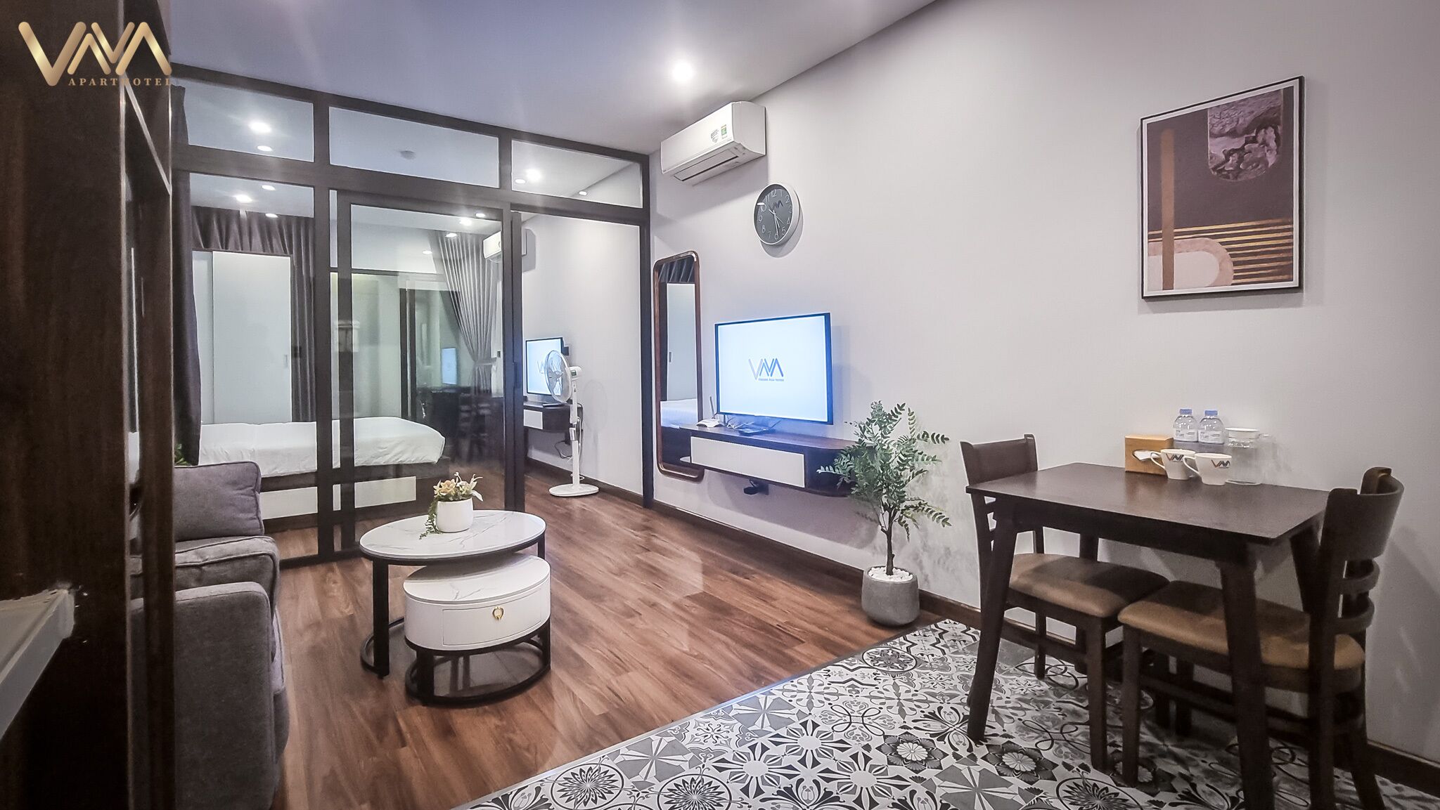 Una sala moderna con un sofá, una mesa redonda de centro, una mesa de comedor con sillas, un televisor y una planta en maceta.