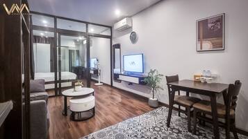 A modern living room with a sofa, a round coffee table, a dining table with chairs, a TV, and a potted plant.