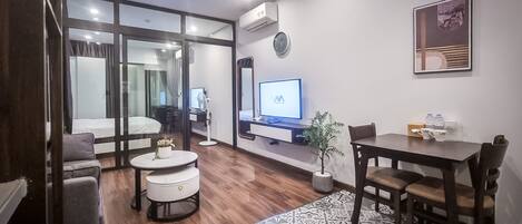 Uma sala de estar moderna com um sofá, uma mesa de centro redonda, uma mesa de jantar com cadeiras, uma TV e um vaso com planta.