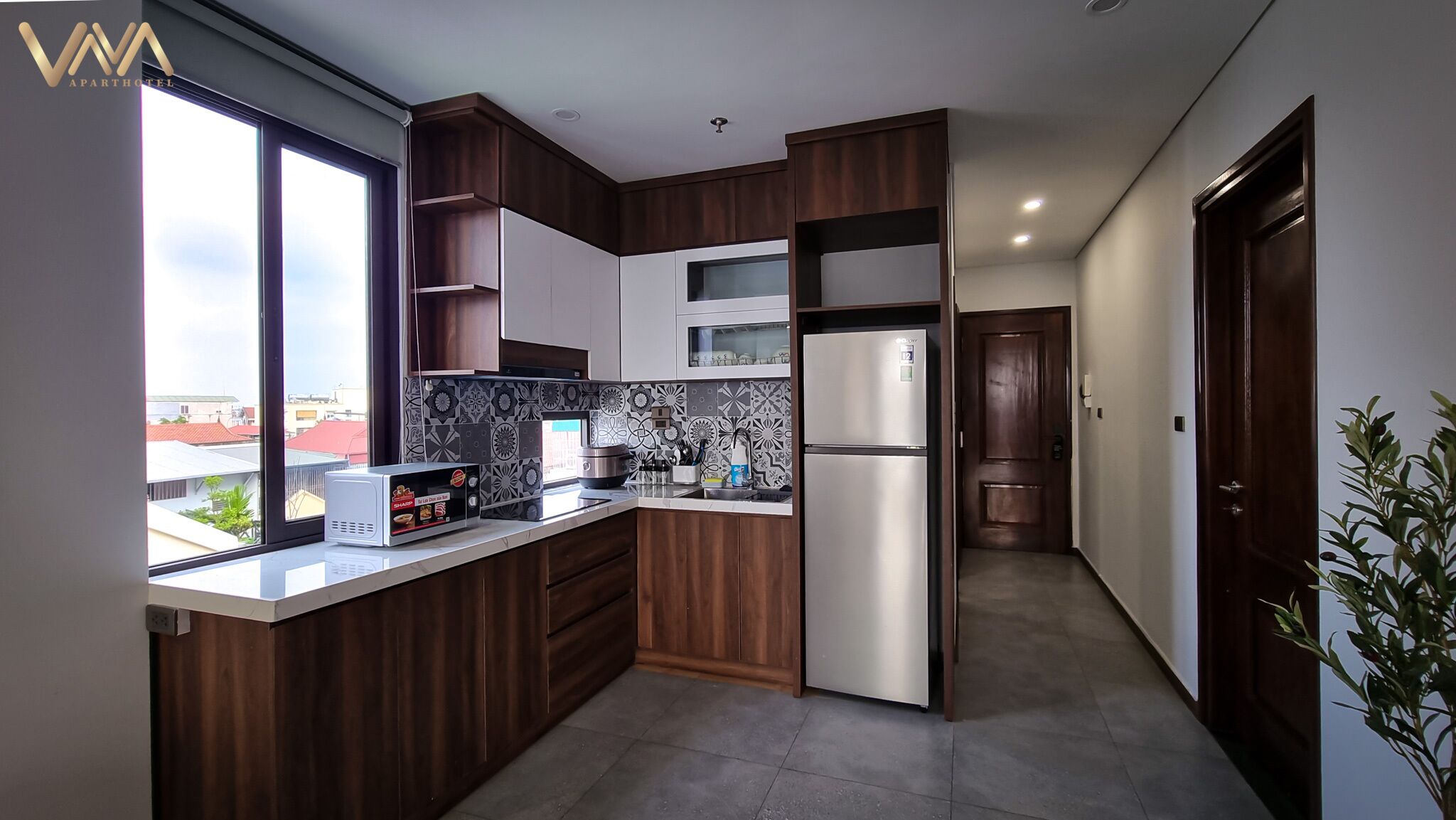 A modern kitchen with wooden cabinets, a stainless steel refrigerator, and a window overlooking a cityscape.