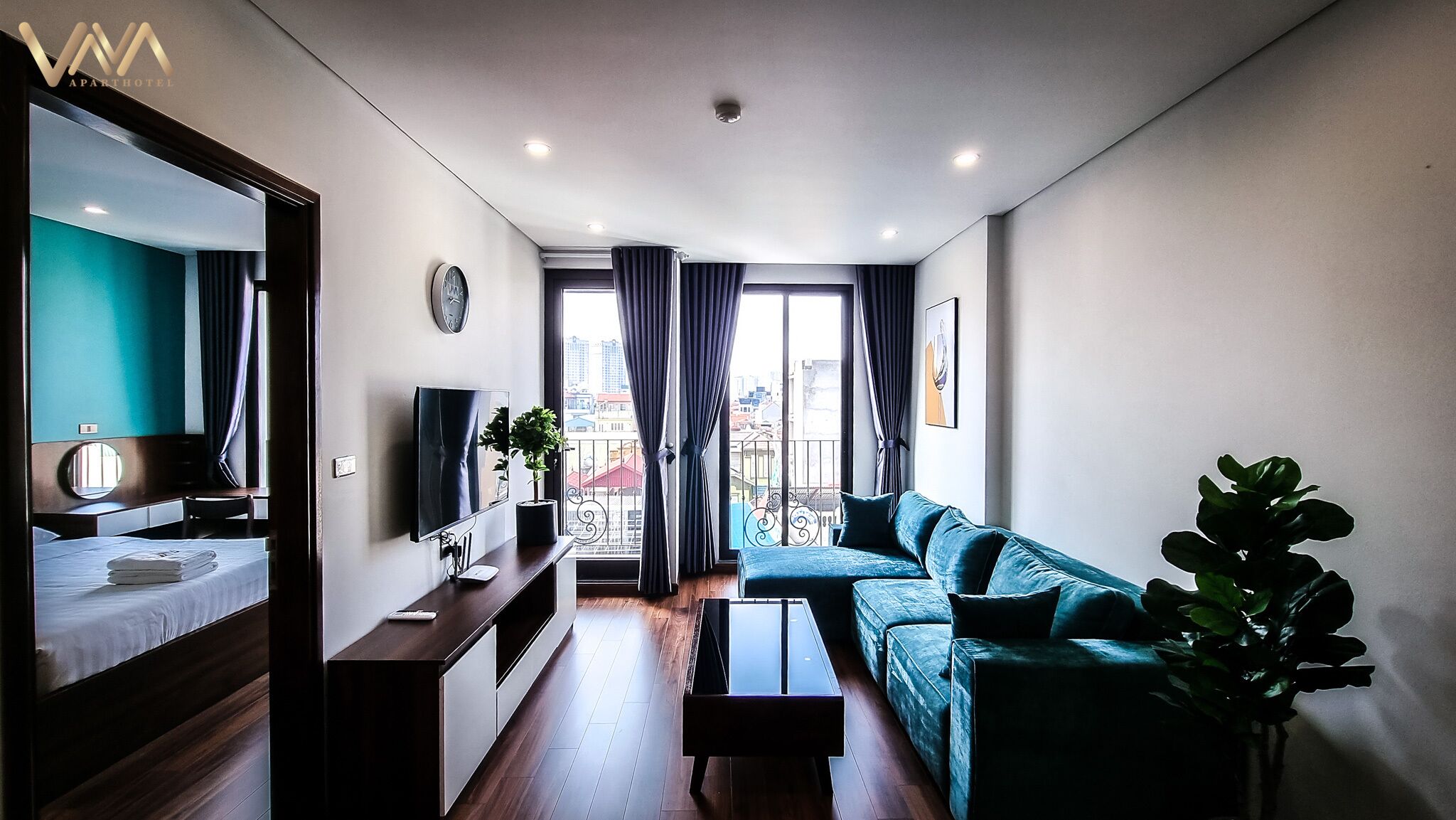 A modern apartment with a bed, a sofa, a TV, a dining table, and a balcony with a view of the city.
