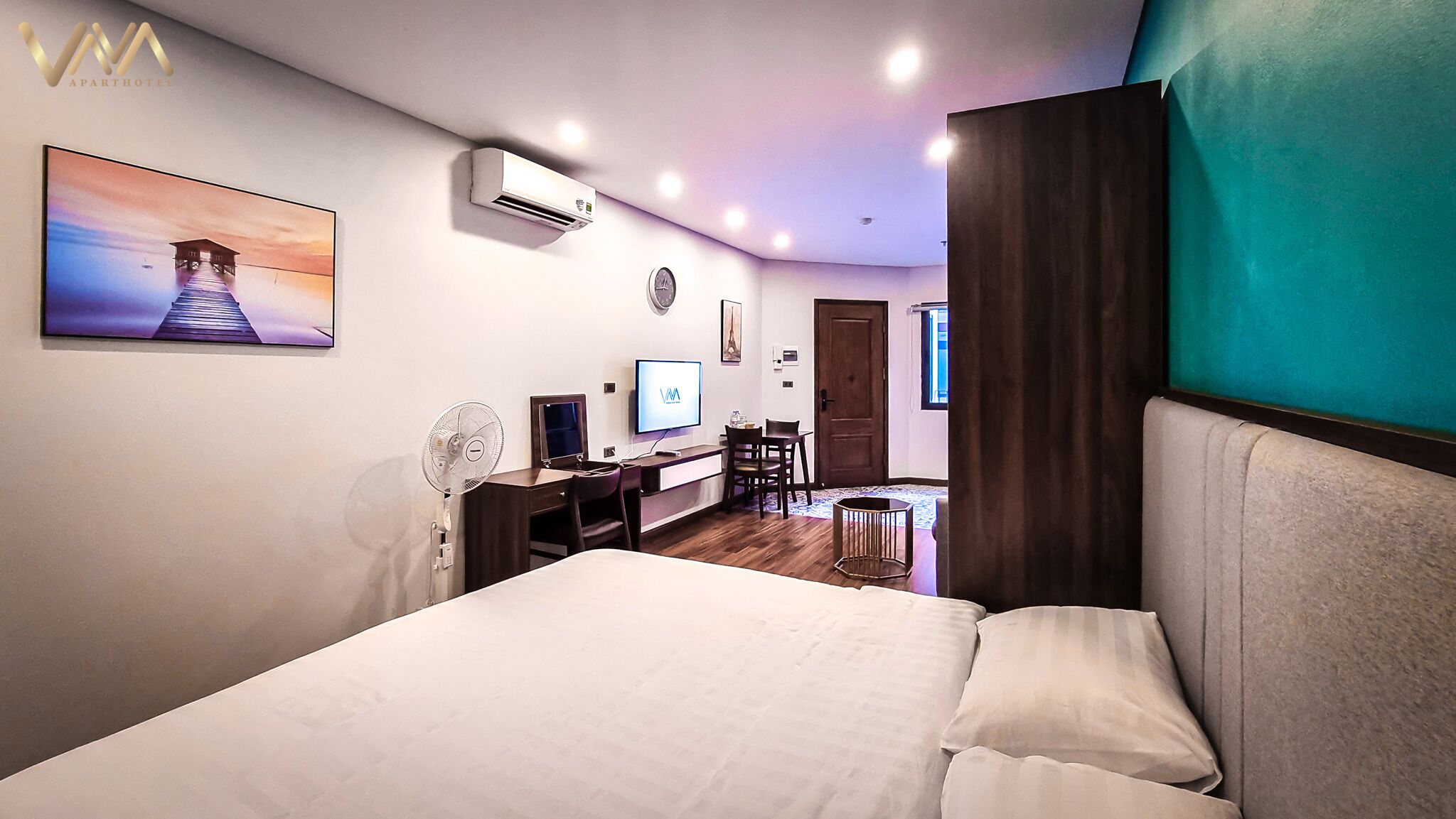 A modern hotel room with a bed, a desk, a chair, a TV, and a wall-mounted air conditioner.