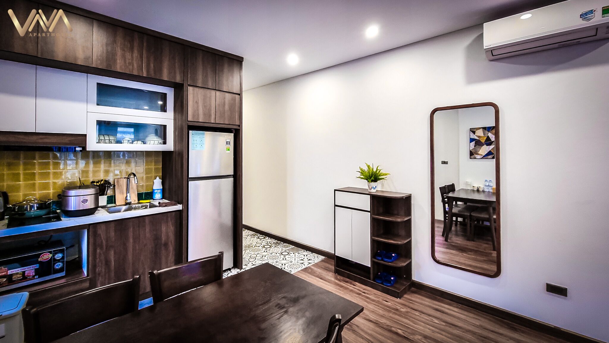 A compact kitchen with modern appliances, a dining area with a wooden table, and a small side table with a plant.