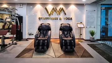 Una palestra con due poltrone massaggianti, attrezzature per esercizi e un cartello con la scritta “GYMFITNESS & YOGA”.