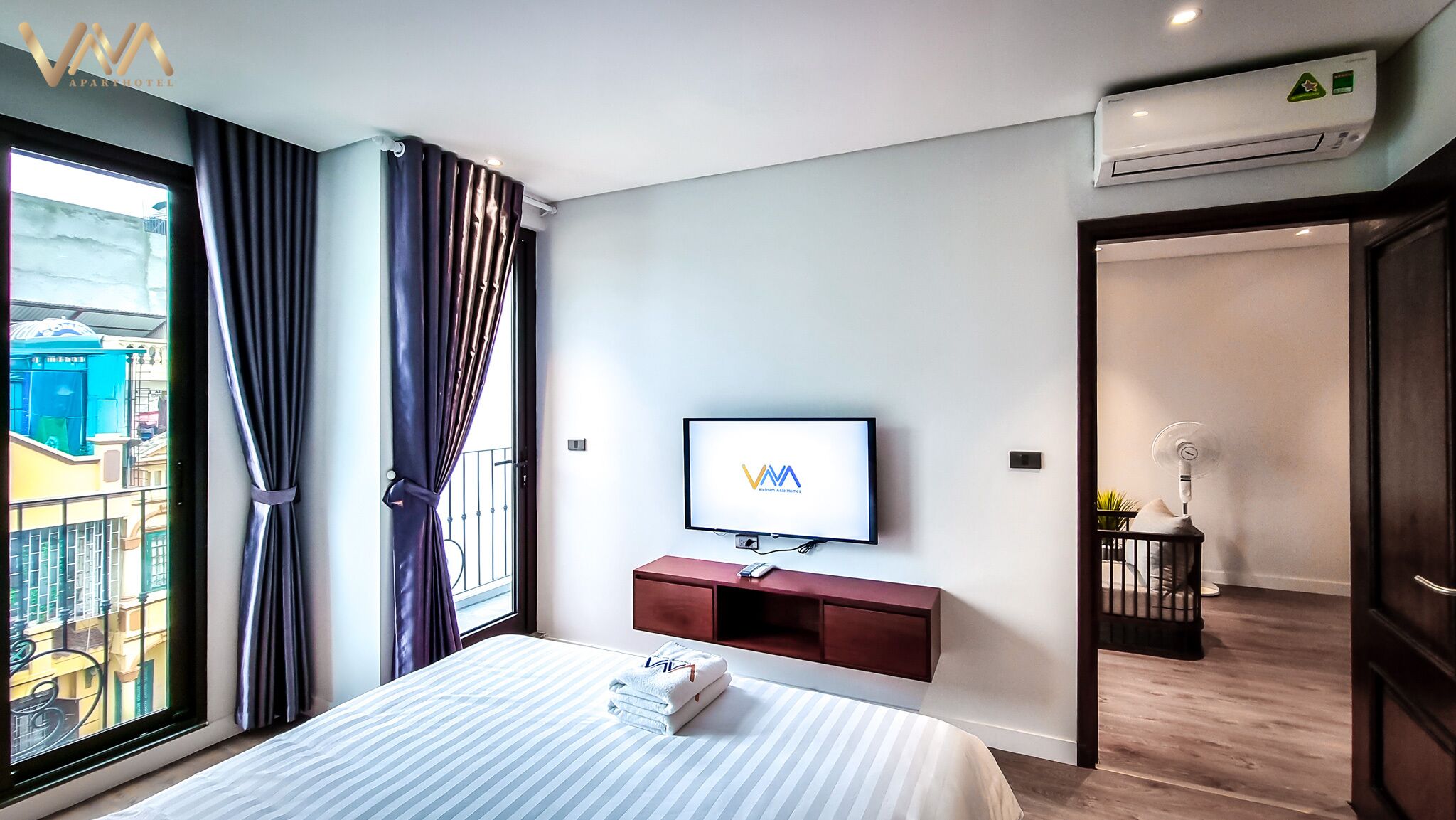 Habitación de hotel con cama, televisión, aire acondicionado y vistas a la ciudad.