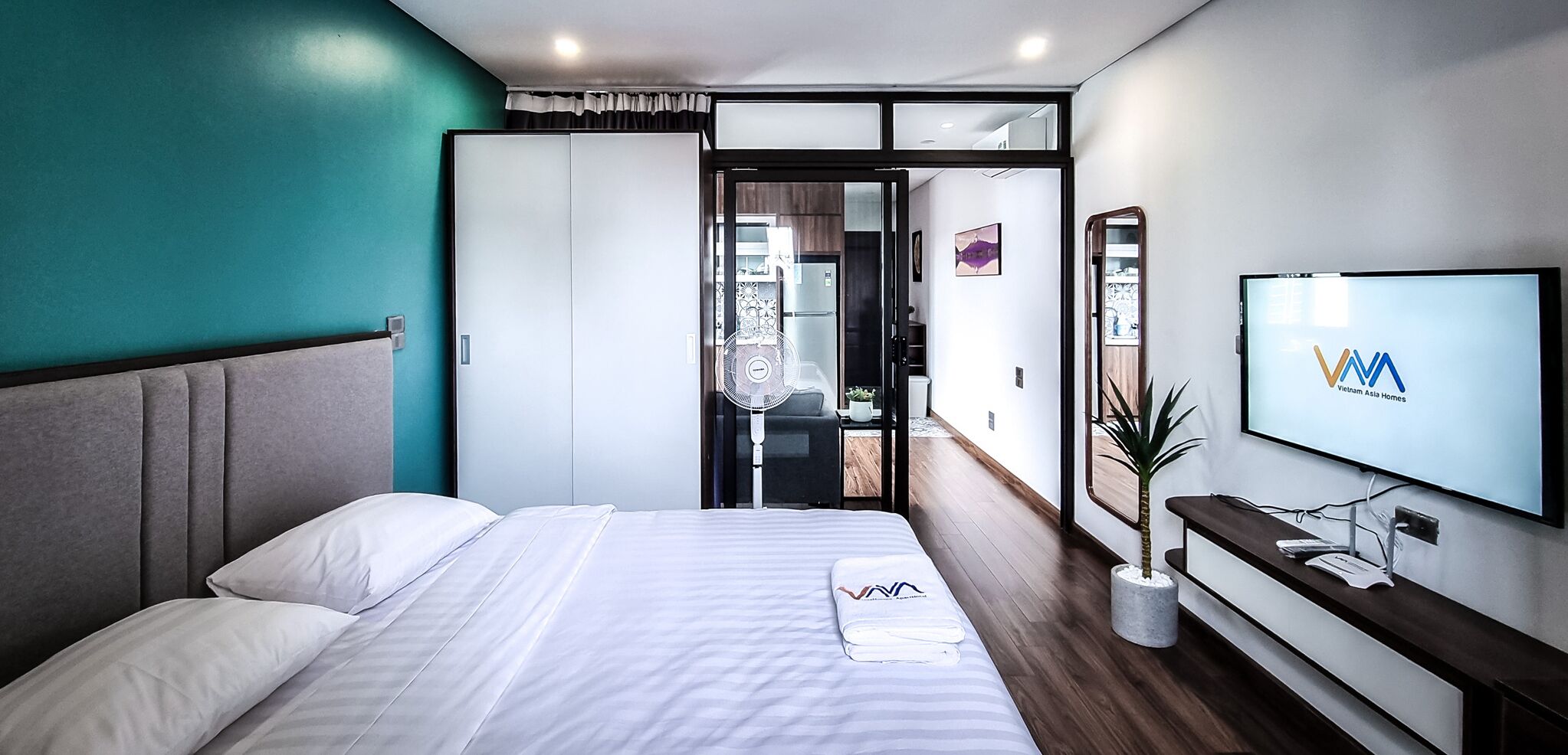 A modern hotel room with a large bed, a TV, and a view into the living area.