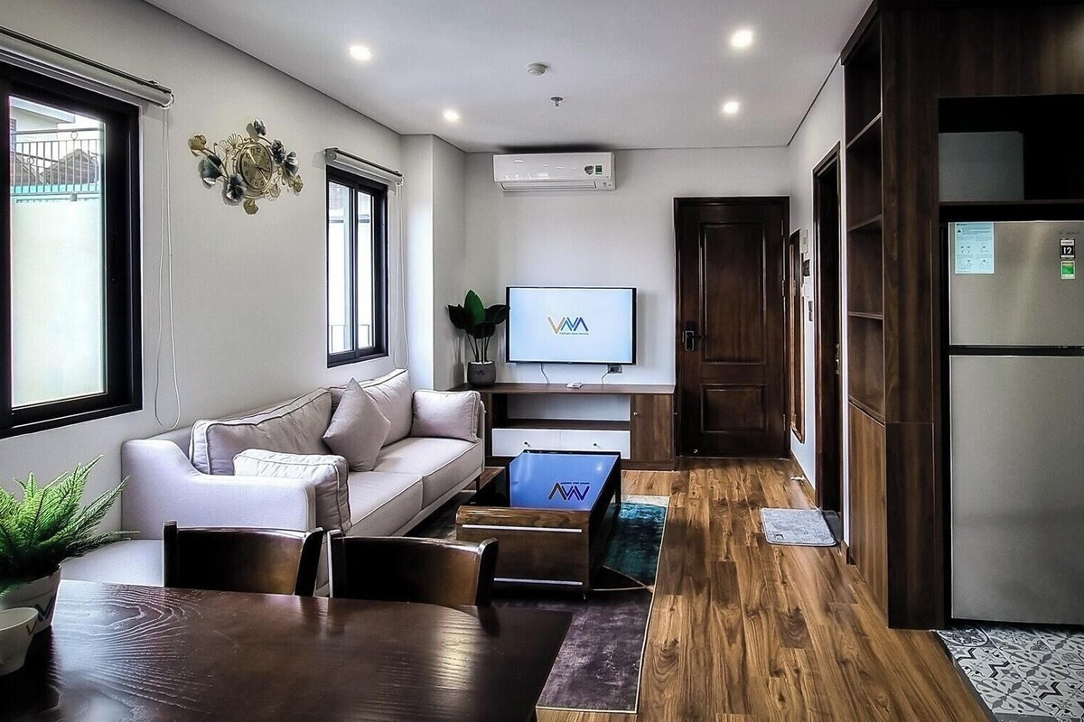 A modern living room with a sofa, coffee table, and a TV. There is a wooden floor, a potted plant, and a window with a view.