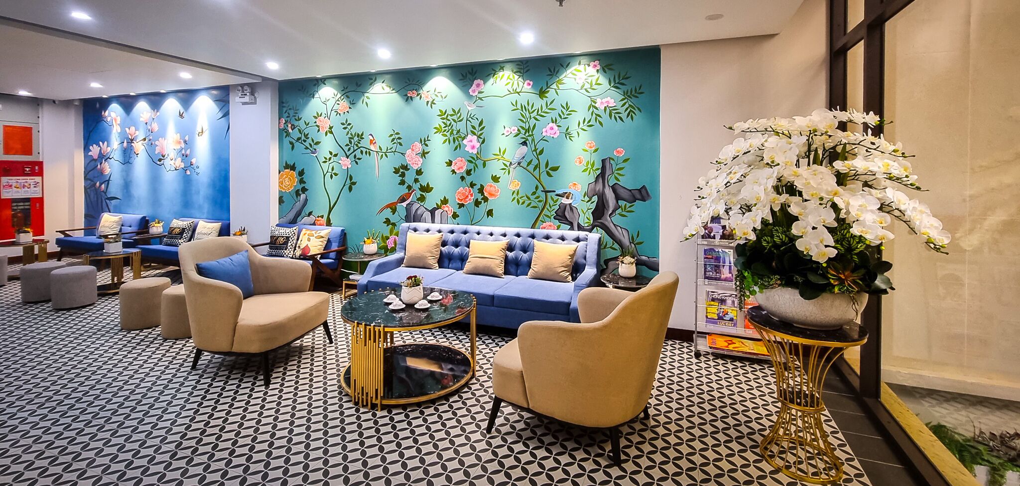 Un vestíbulo de hotel con un sofá azul, sillones color beige, una mesa de centro redonda y un suelo con diseño.