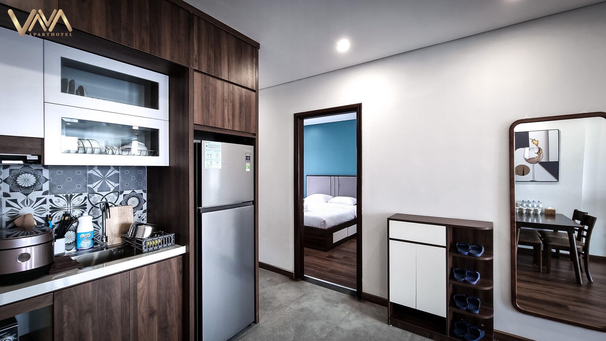 Ein kleines Hotelzimmer mit Küchenzeile, einem Bett, einer Essecke und einem Spiegel.