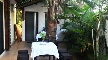 A small outdoor dining area with a table set for two, surrounded by tropical plants and a palm tree.